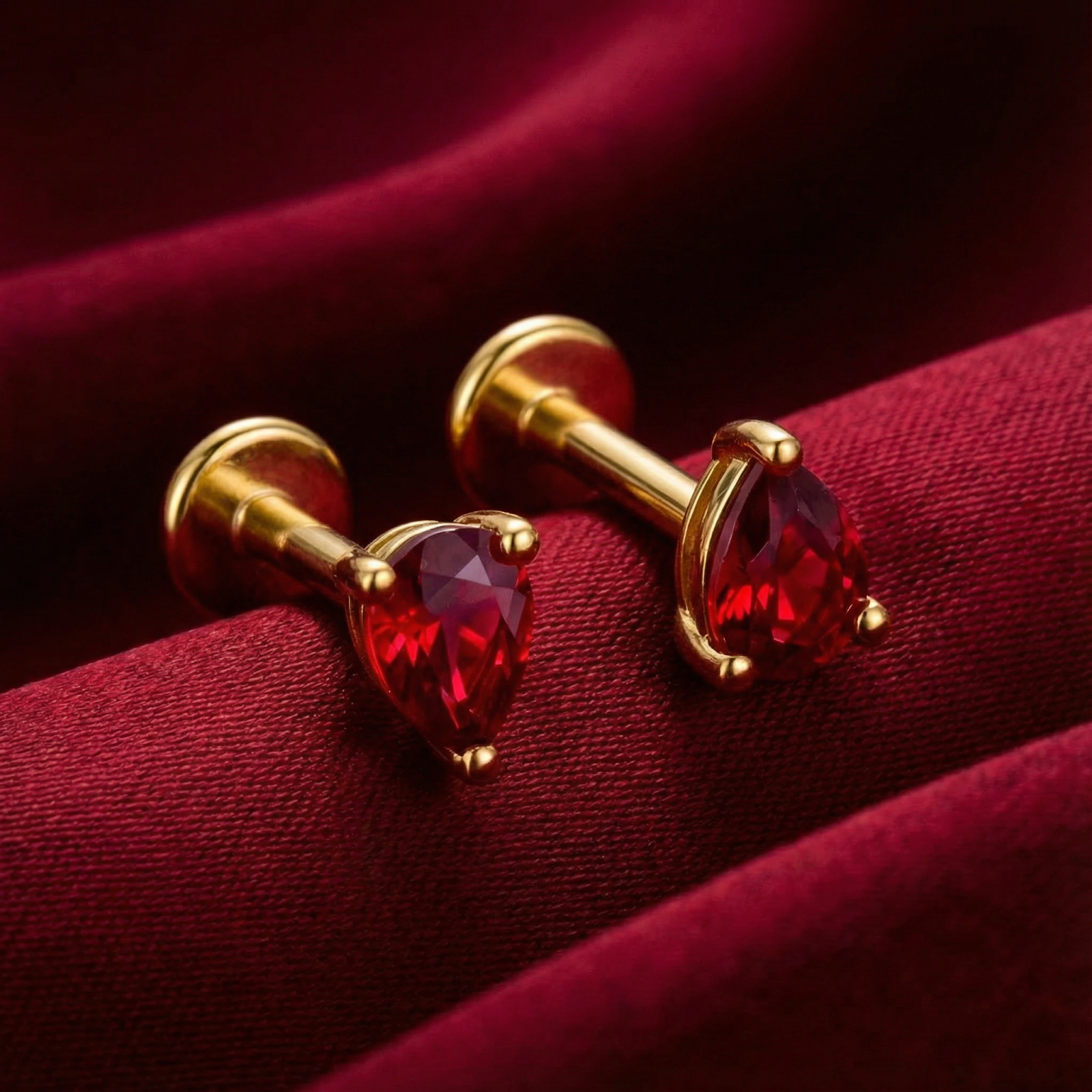 Side view of pear-shaped simulated ruby earrings with 18K gold vermeil posts on red satin.