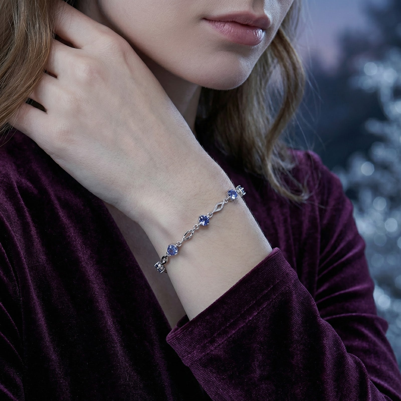 Side view of a woman wearing a sterling silver station bracelet with round blue simulated tanzanite stones.