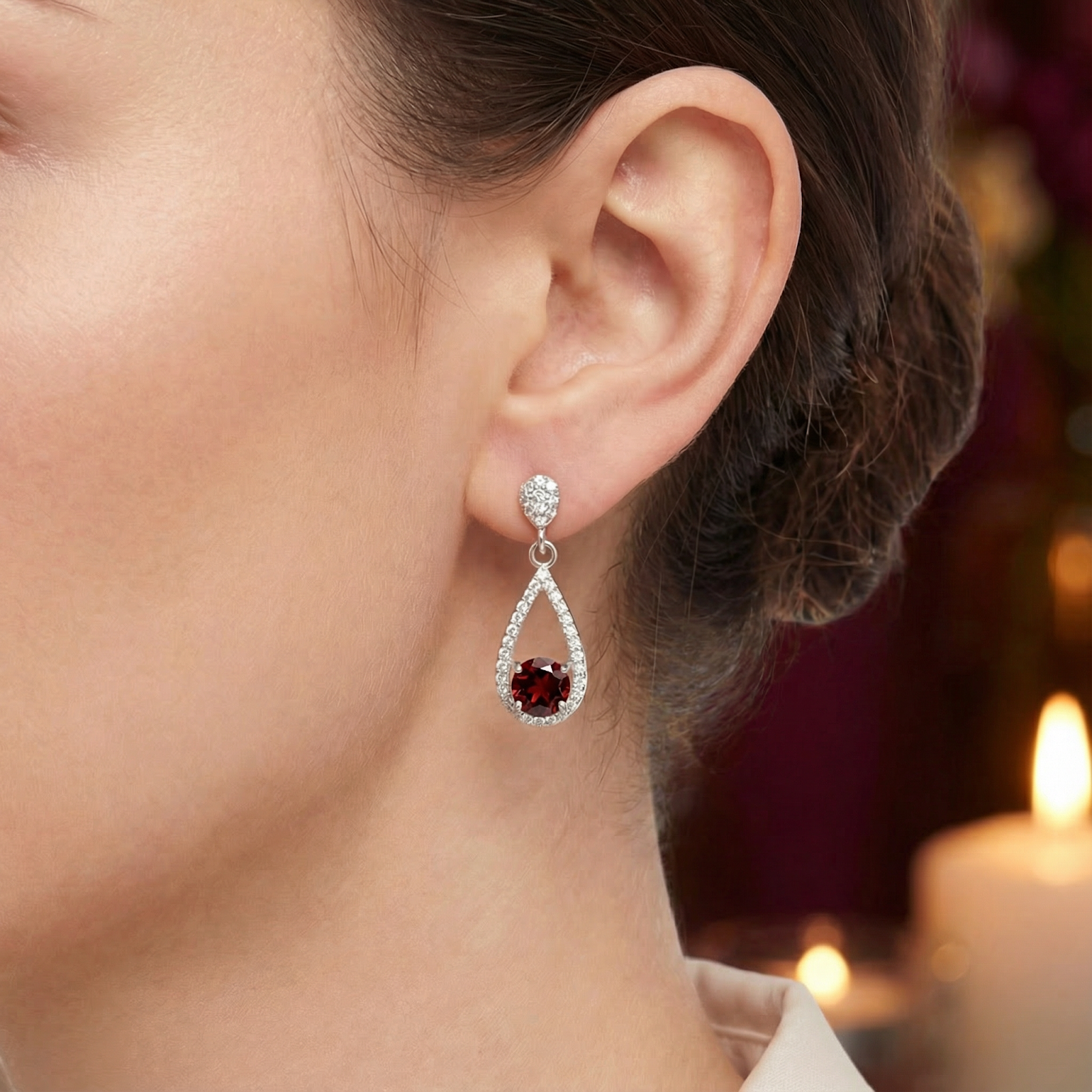 Close-up of a simulated garnet teardrop earring in sterling silver worn on a model's ear with candle light.