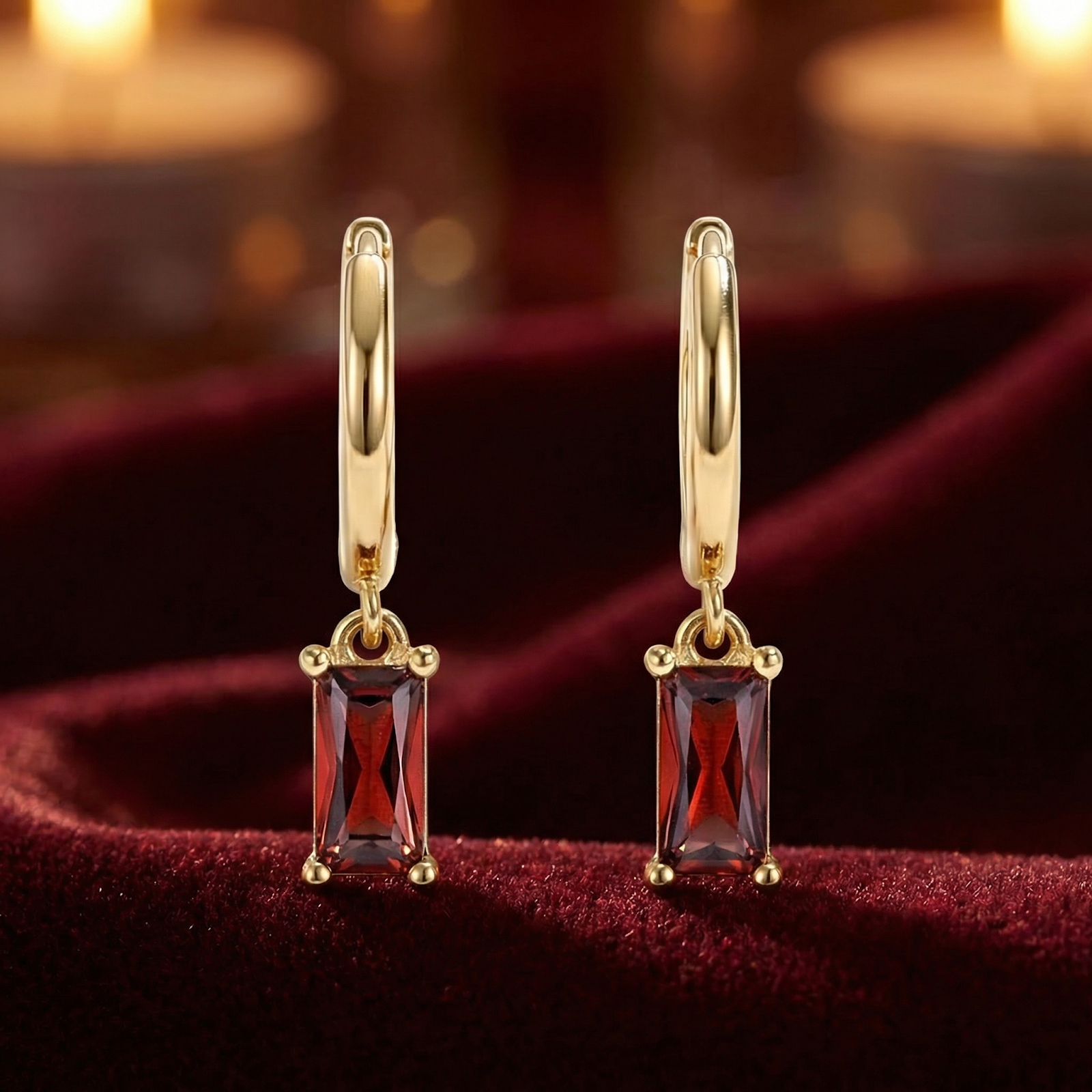 Front view of 18K gold vermeil huggie earrings with emerald-cut simulated garnet stones on red velvet.