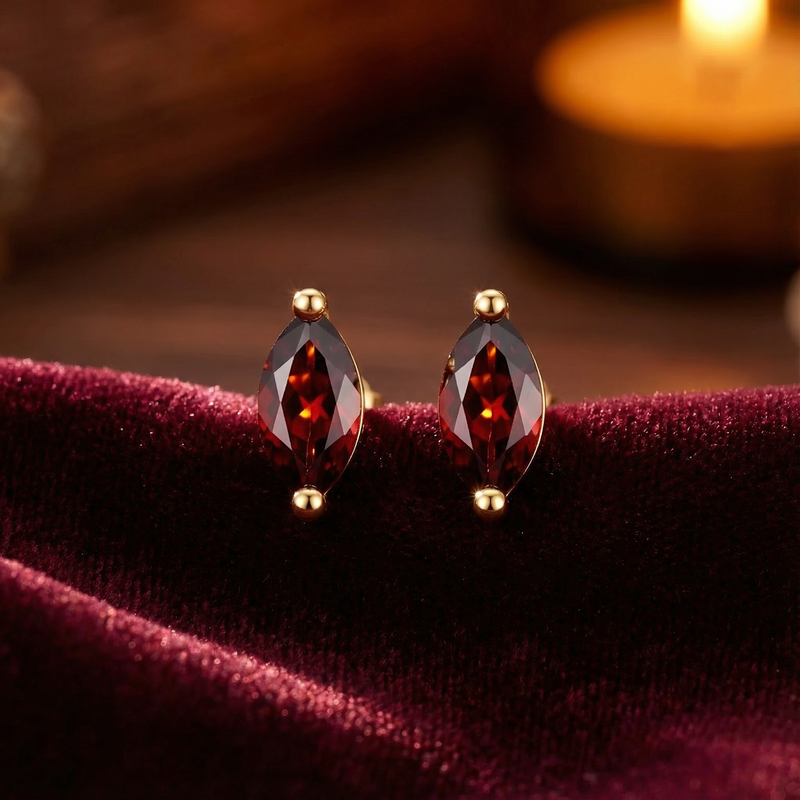 Frontal view of marquise cut simulated garnet stud earrings in 18K gold vermeil on a red velvet background.