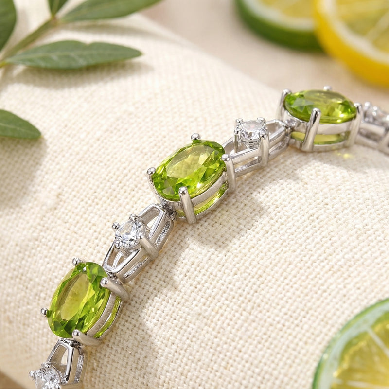 Close-up of oval-cut simulated peridot stones in a S925 sterling silver prong setting on a station bracelet.