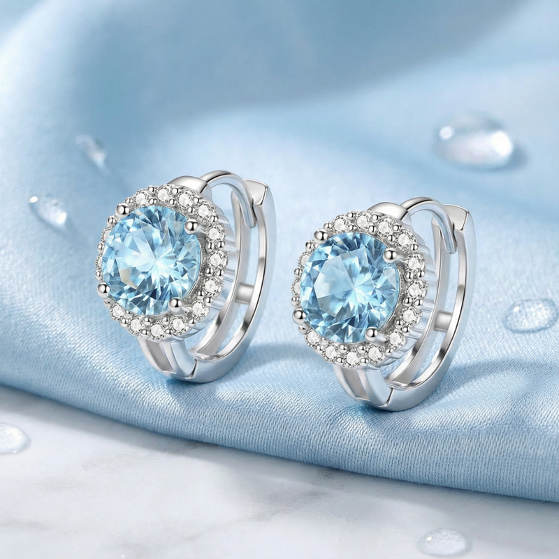 Detail of round cut light blue simulated aquamarine halo earrings with sterling silver leverback settings.