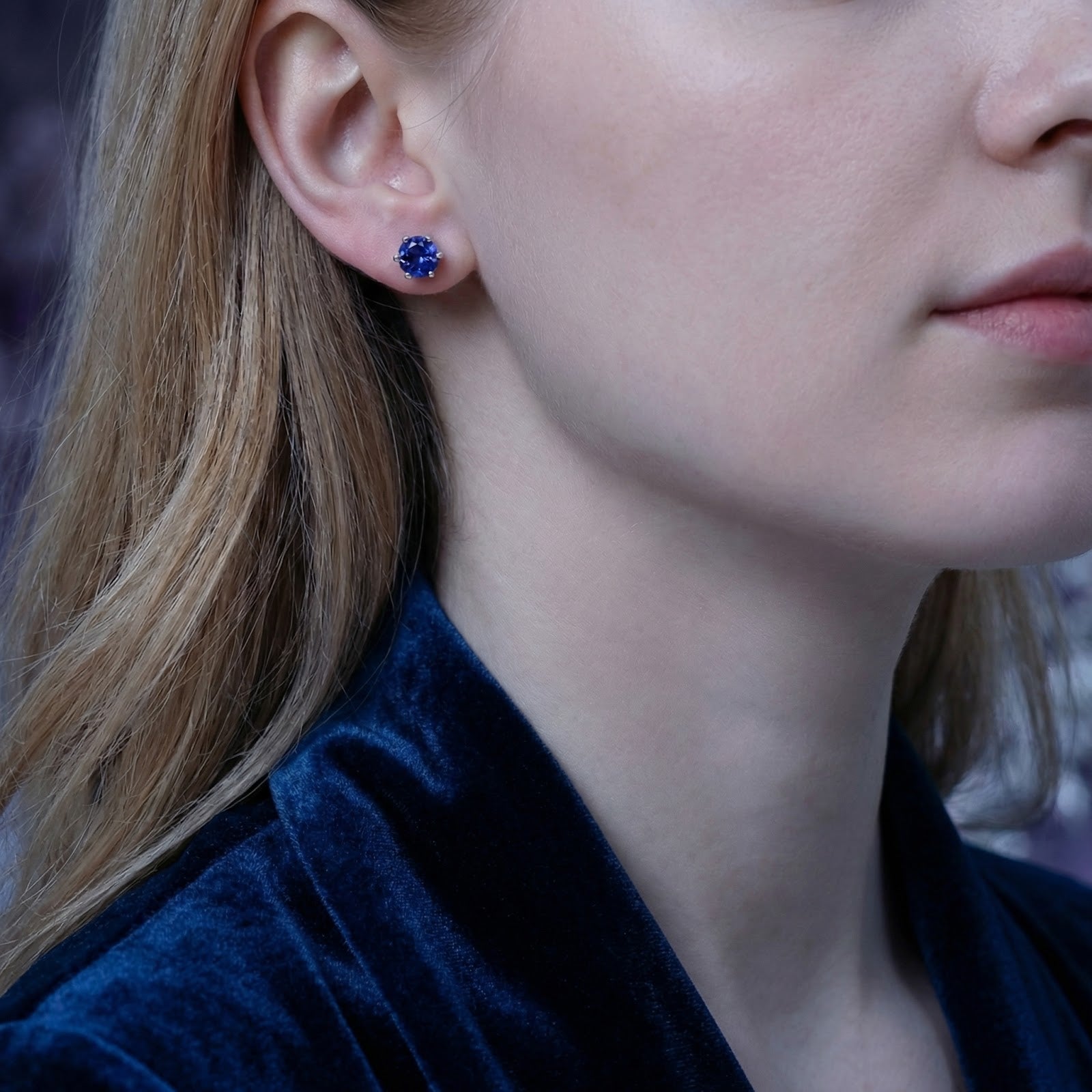 Model wearing a round simulated tanzanite stud earring in S925 sterling silver on her earlobe.