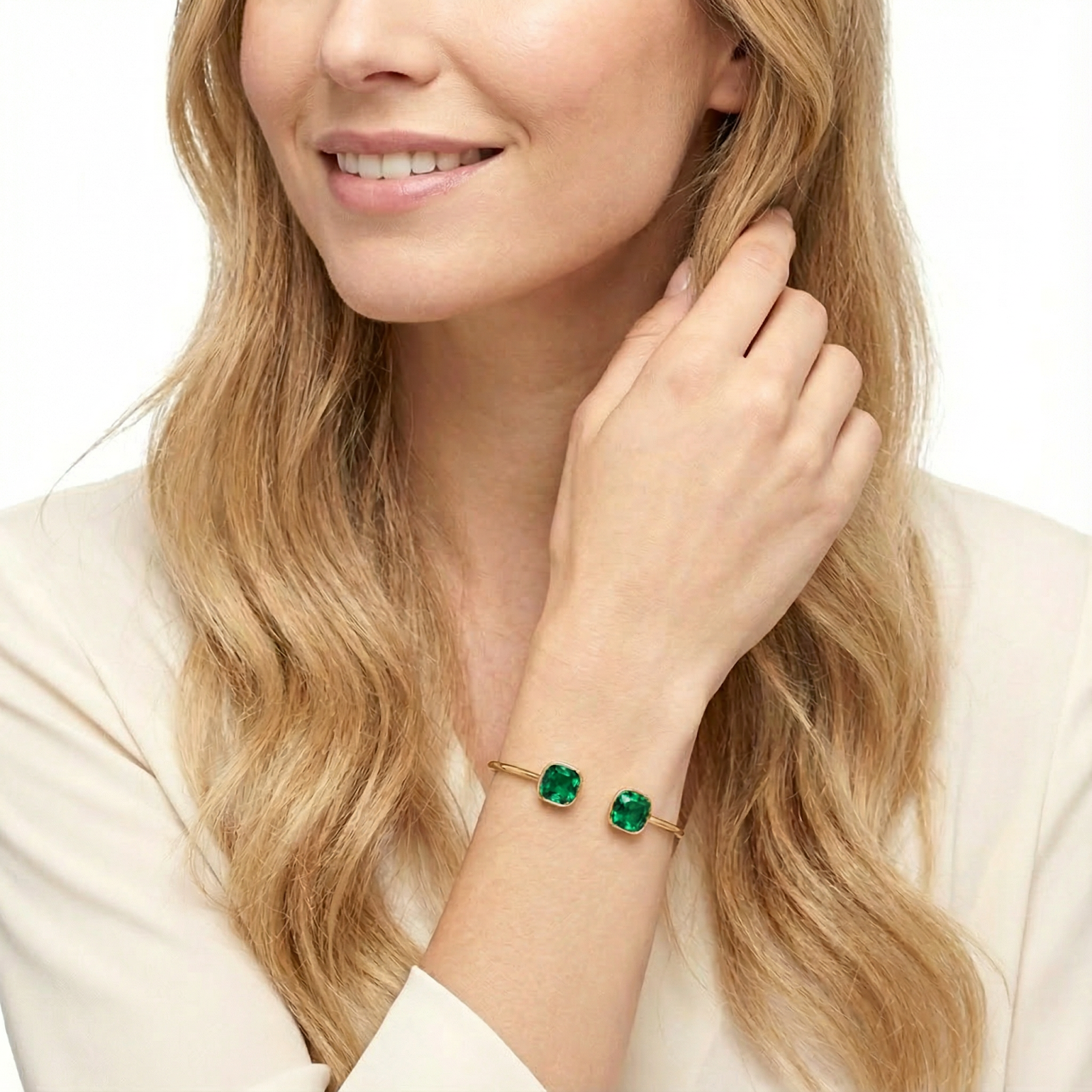 Gold finish stainless steel bypass cuff bracelet with cushion cut simulated emeralds on a model's wrist.