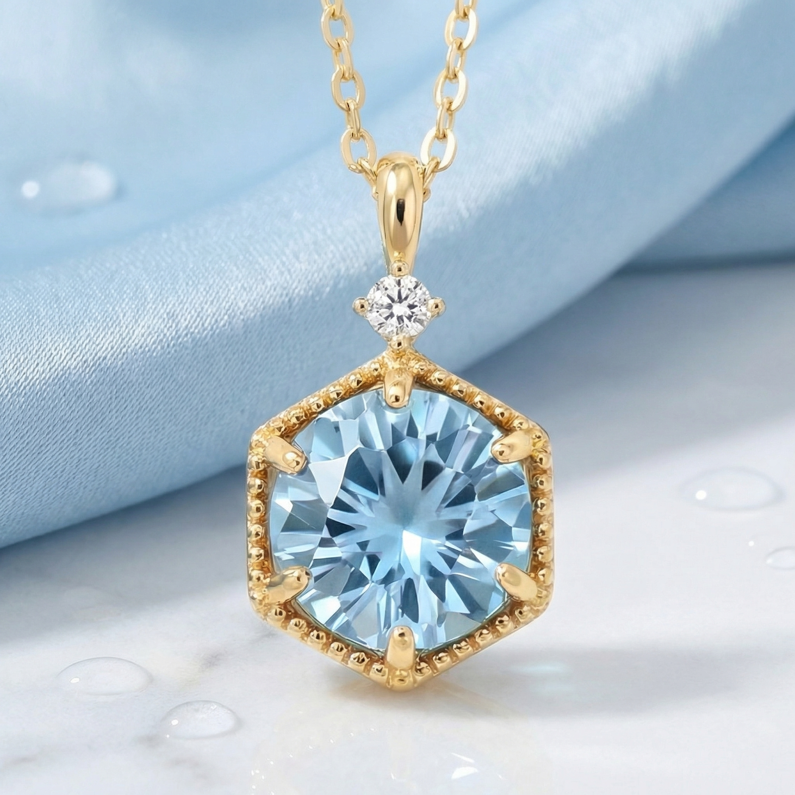 Hexagon cut simulated aquamarine necklace in 18K gold vermeil, macro view on light blue fabric.