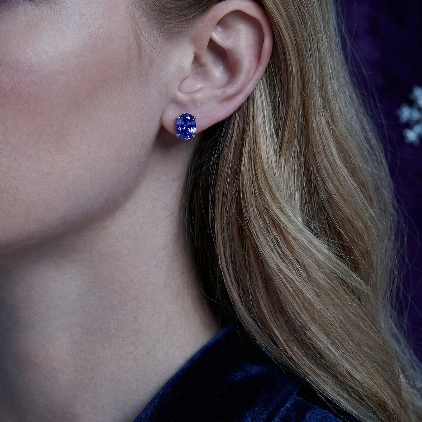 Model wearing an oval cut simulated tanzanite stud earring in sterling silver, showing the earring's scale.