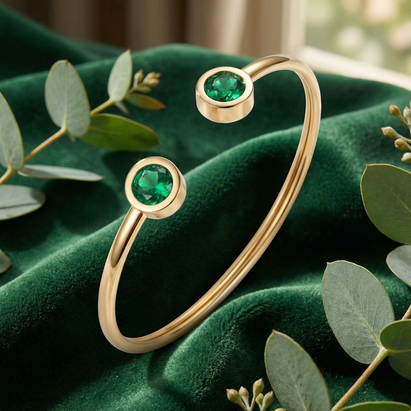 Gold stainless steel bypass cuff bracelet with round simulated emeralds on a green velvet lifestyle background.
