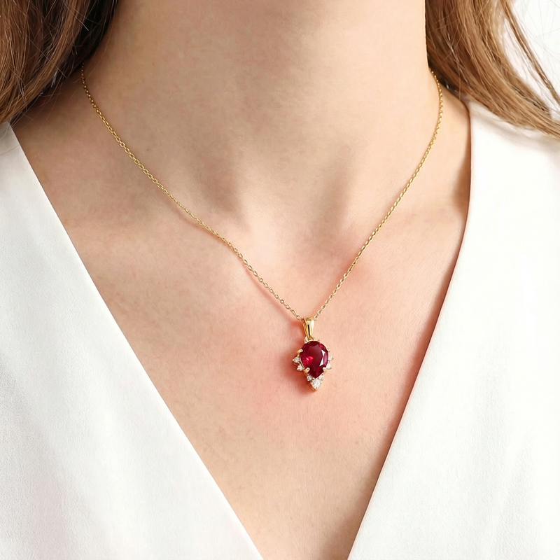 Close-up of the pear cut simulated ruby birthstone necklace in 18K gold vermeil on a model's neck.