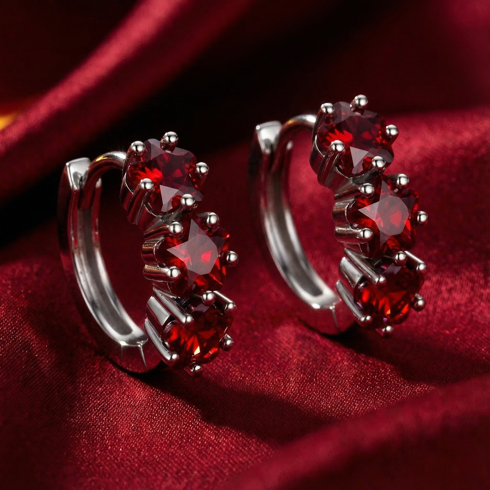 Star-cut simulated ruby huggie earrings in S925 sterling silver displayed on red silk fabric.