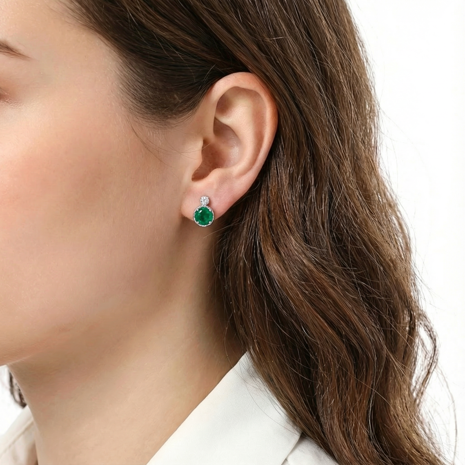 Brunette model wearing a round-cut simulated emerald and S925 sterling silver halo stud earring.