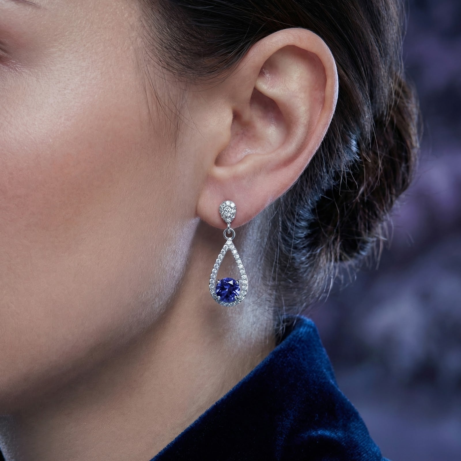Side view of a model wearing the sterling silver Myrenis teardrop earring with blue simulated tanzanite.