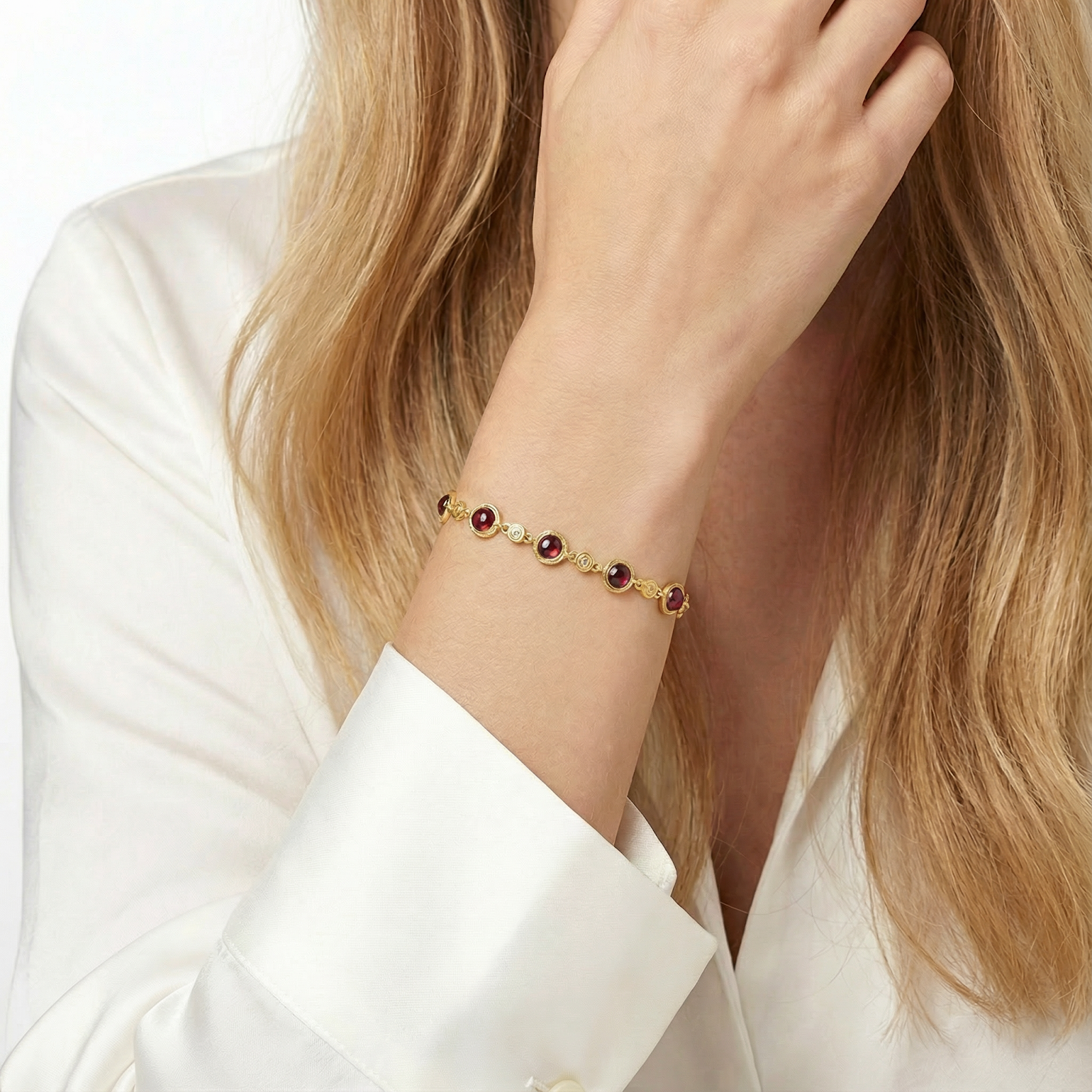 18K gold vermeil station bracelet with round simulated garnets worn on a woman's wrist with a white shirt.