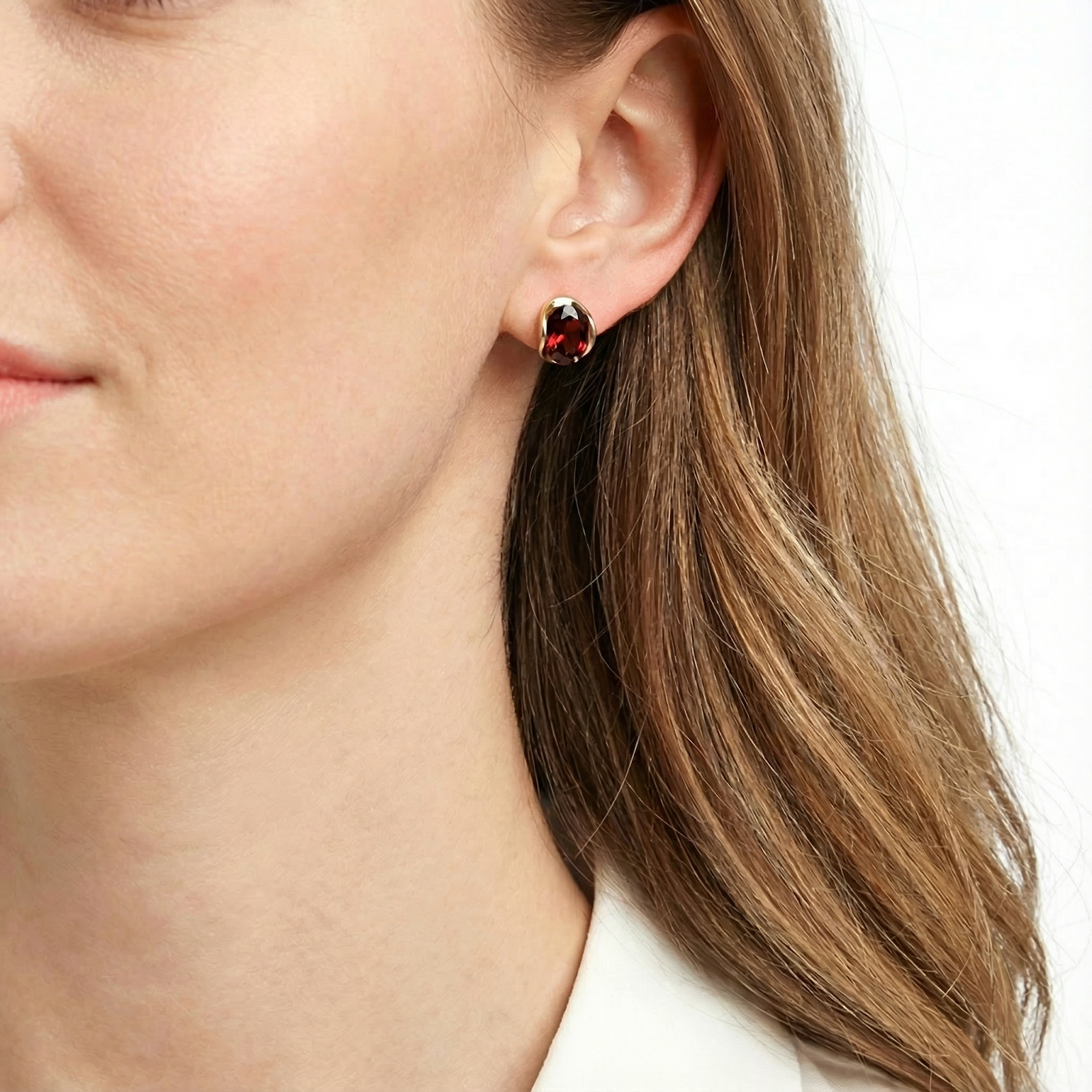 A woman wearing the 18K gold vermeil January birthstone huggie earrings with deep red simulated garnet.
