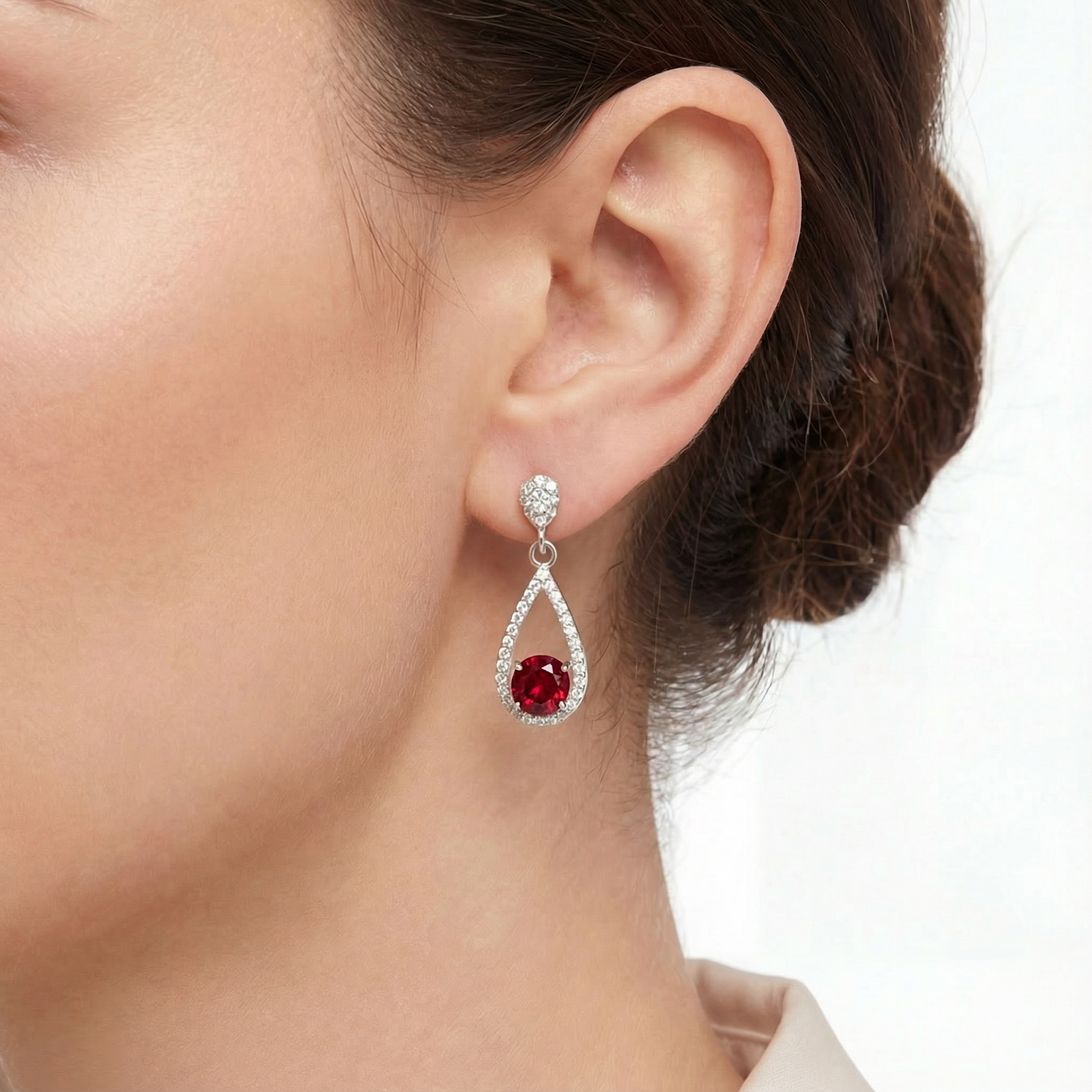 Side view of a teardrop-shaped S925 sterling silver and simulated ruby drop earring worn on an ear.