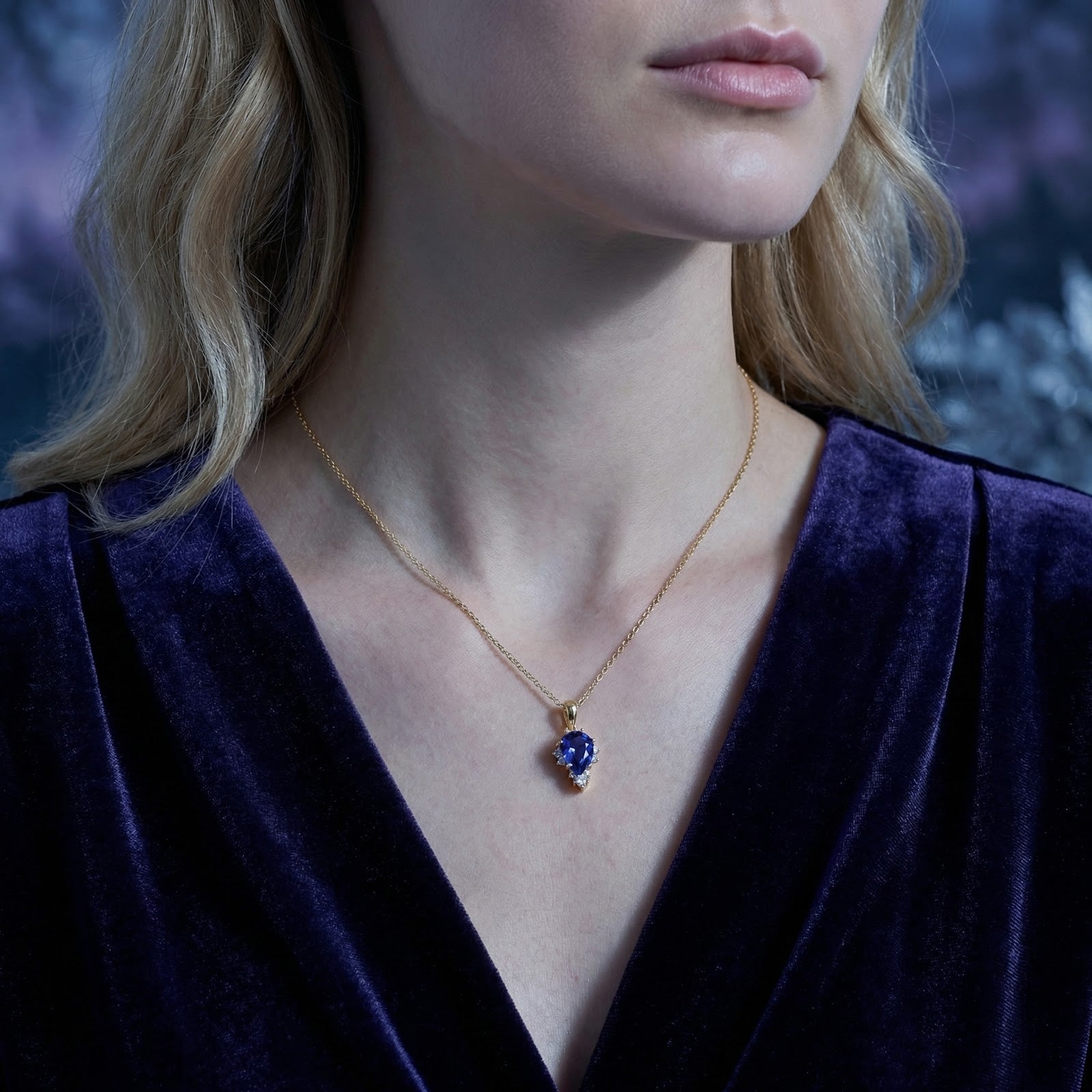 Model wearing the 18K gold vermeil pear-cut simulated tanzanite necklace with a purple velvet V-neck top.