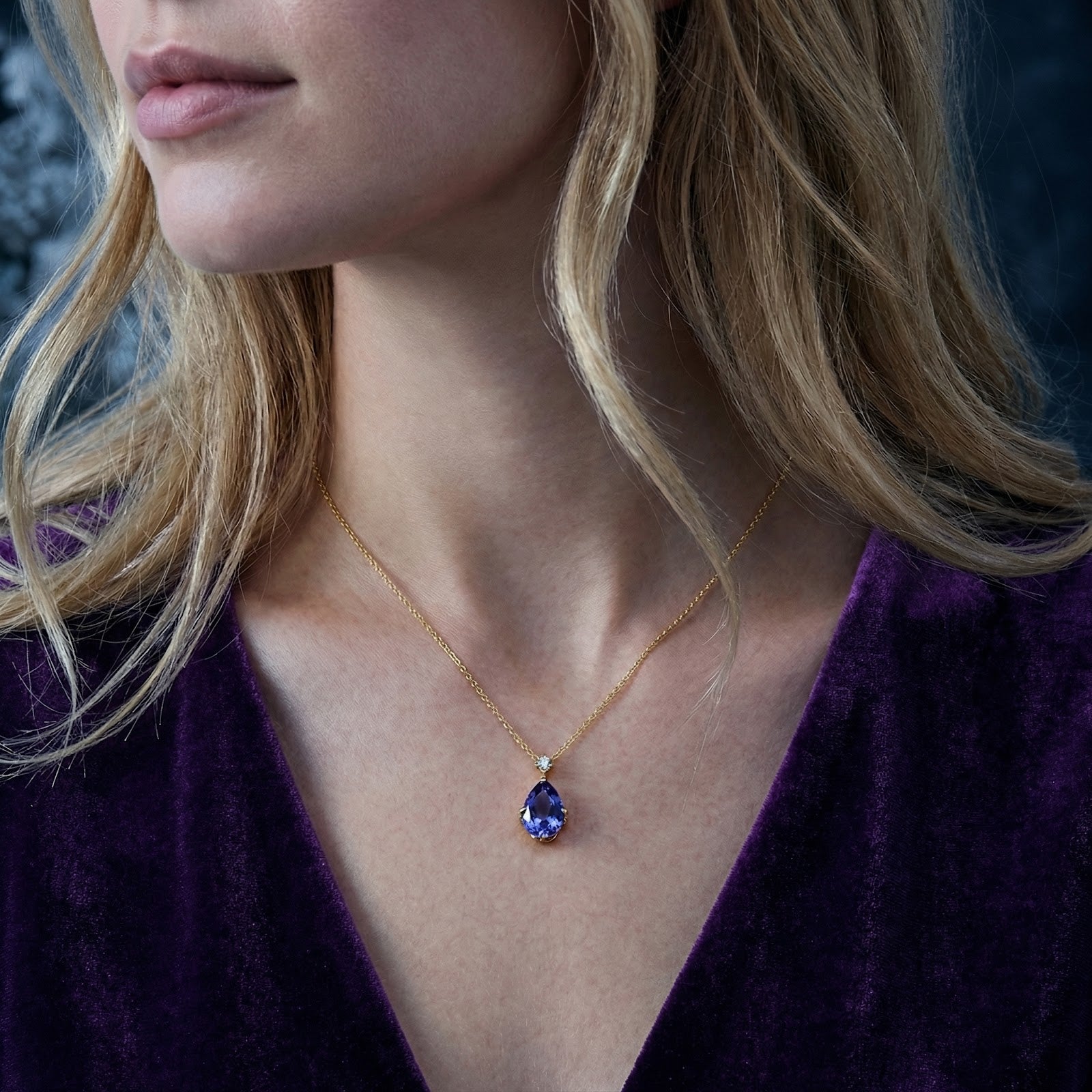 Woman wearing the gold Lyranelle teardrop necklace with a blue-violet simulated tanzanite pendant.