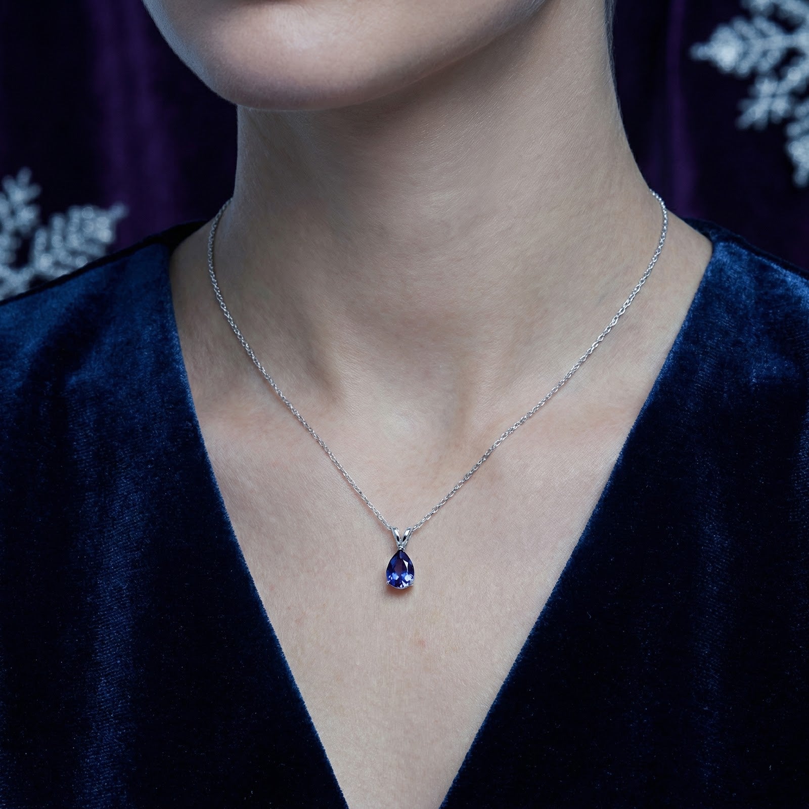 Model wearing the pear-cut blue moissanite necklace in S925 sterling silver against a dark blue velvet dress.