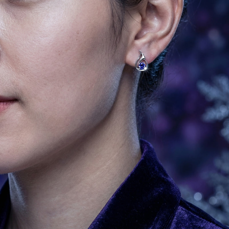 A woman wearing the sterling silver Florisara Bud stud earring with a round-cut blue simulated tanzanite.
