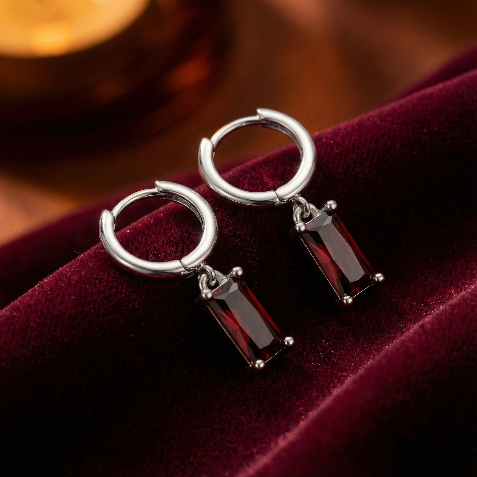 S925 sterling silver huggie earrings with emerald-cut simulated garnet stones on red velvet.