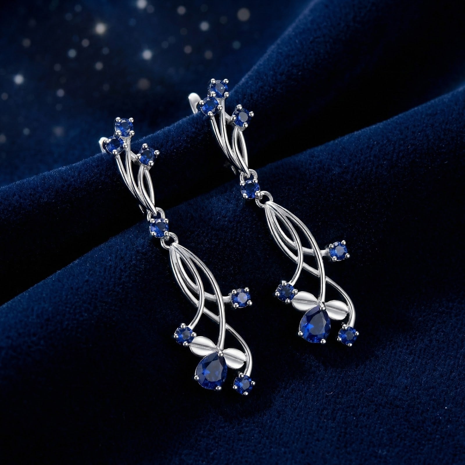 Nerise vine drop earrings in S925 sterling silver with pear and round cut simulated sapphires on blue velvet.