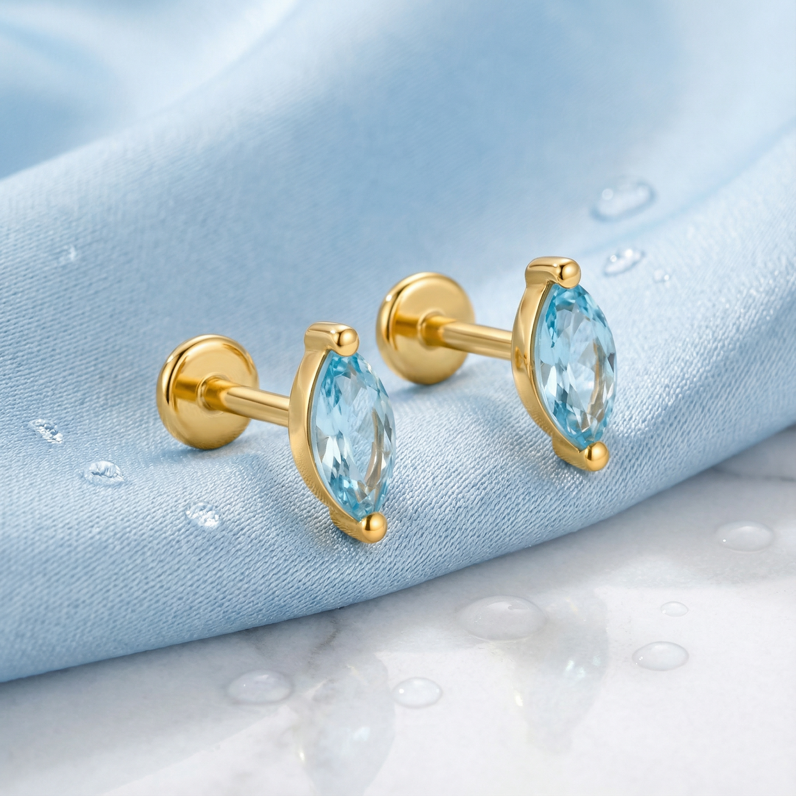 Side view of marquise cut simulated aquamarine earrings in 18K gold vermeil with flat backs on blue silk.