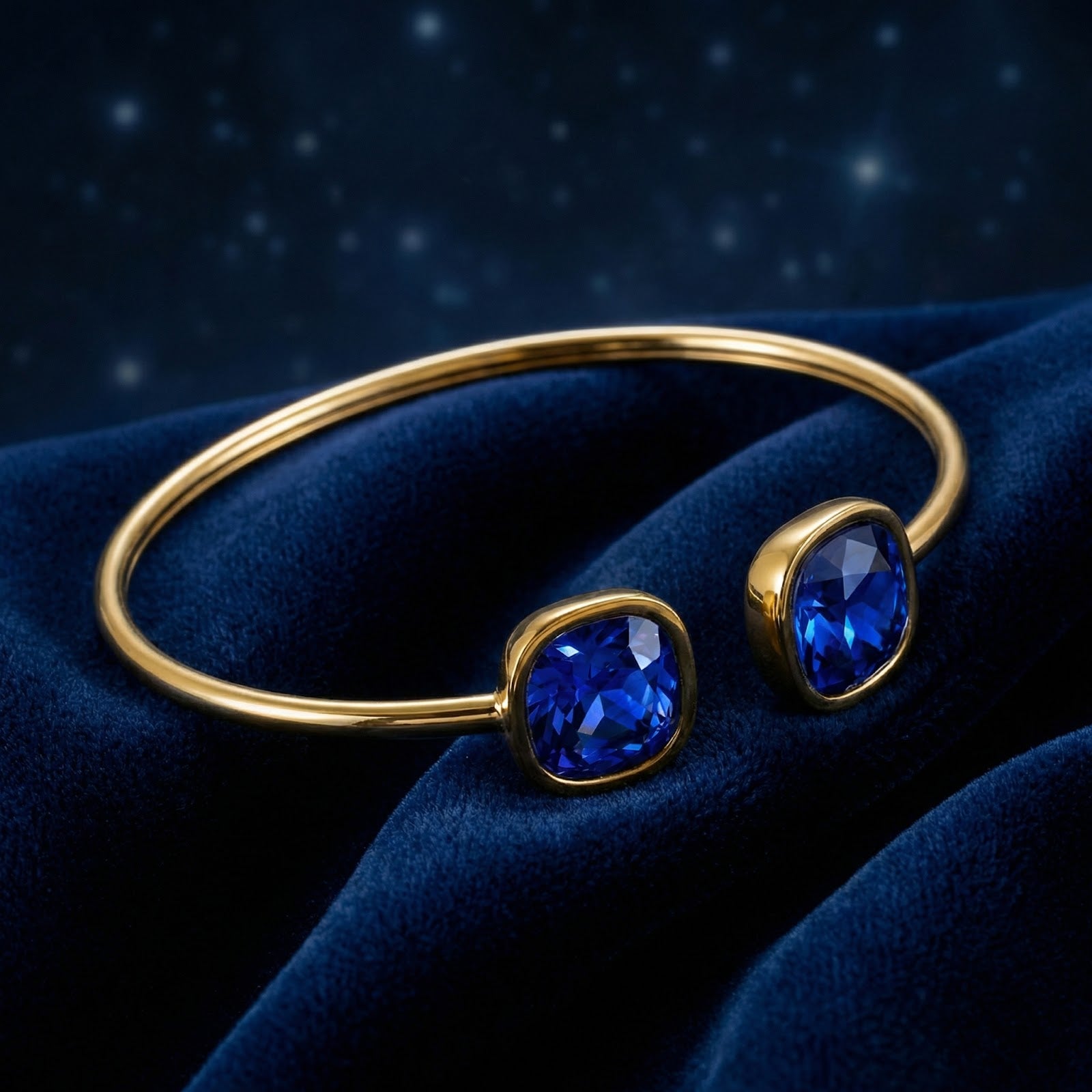 Gold-toned stainless steel cuff bracelet with cushion-cut simulated sapphires on blue velvet.