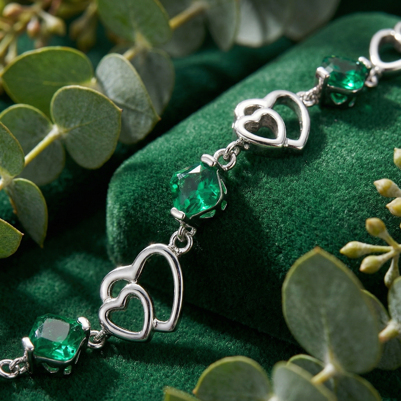 Macro shot of the sterling silver heart links and cushion cut simulated emerald stones on green velvet.