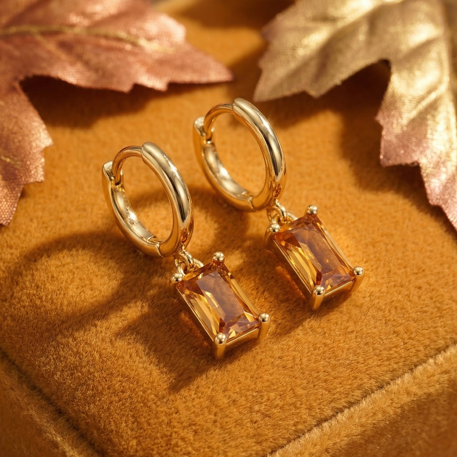 Gold vermeil drop earrings with emerald-cut honey topaz stones on a velvet surface with autumn leaves.