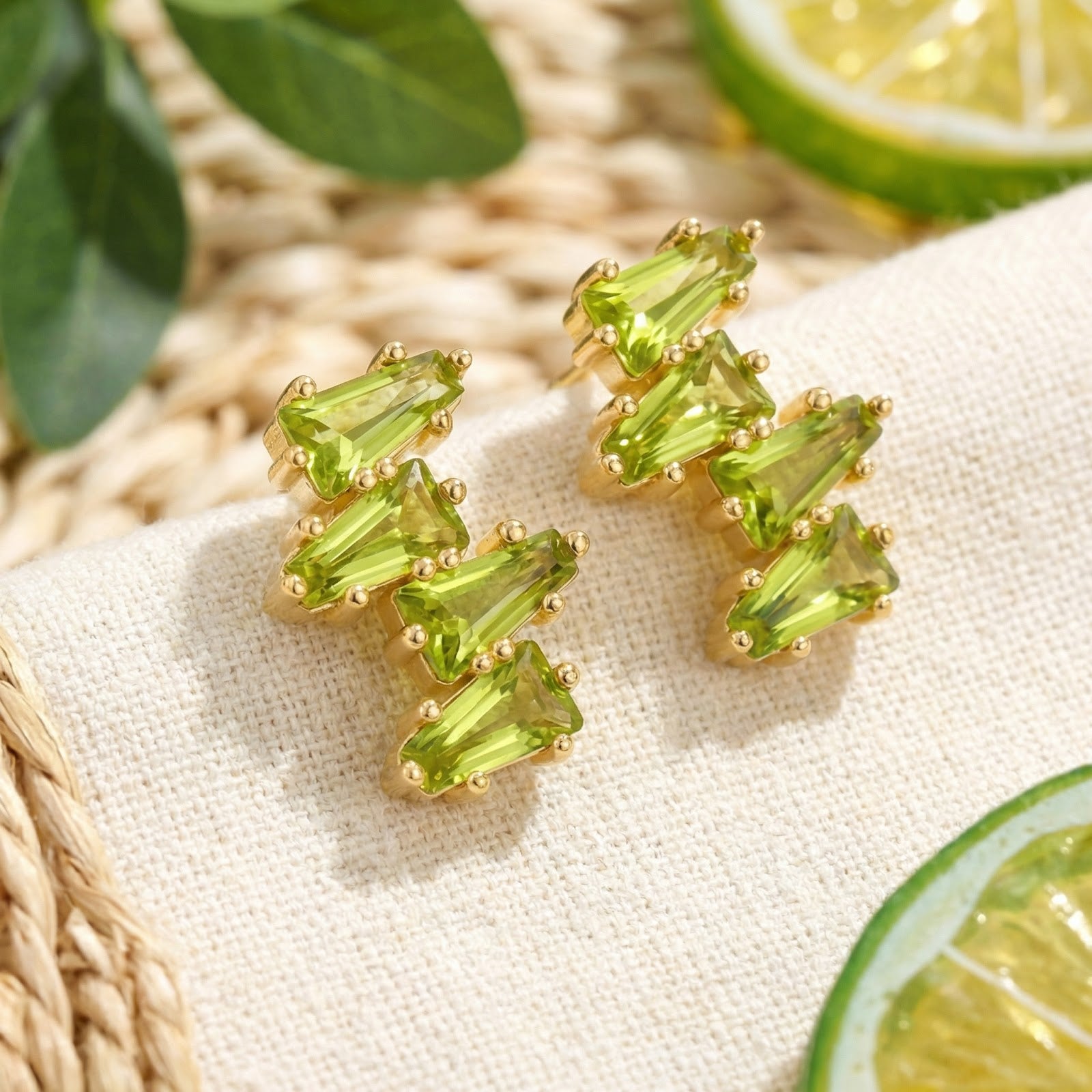 Tapered peridot vine cluster earrings in 18K gold vermeil displayed on white fabric with citrus and leaf accents.