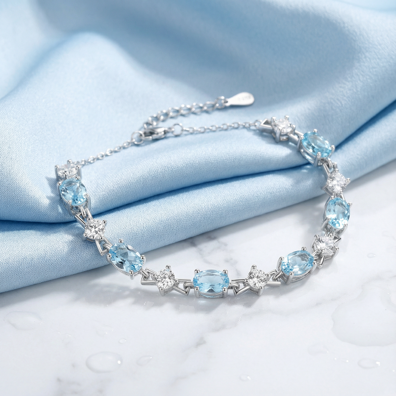 Oval-cut light blue simulated aquamarine station bracelet in sterling silver displayed on draped blue silk.