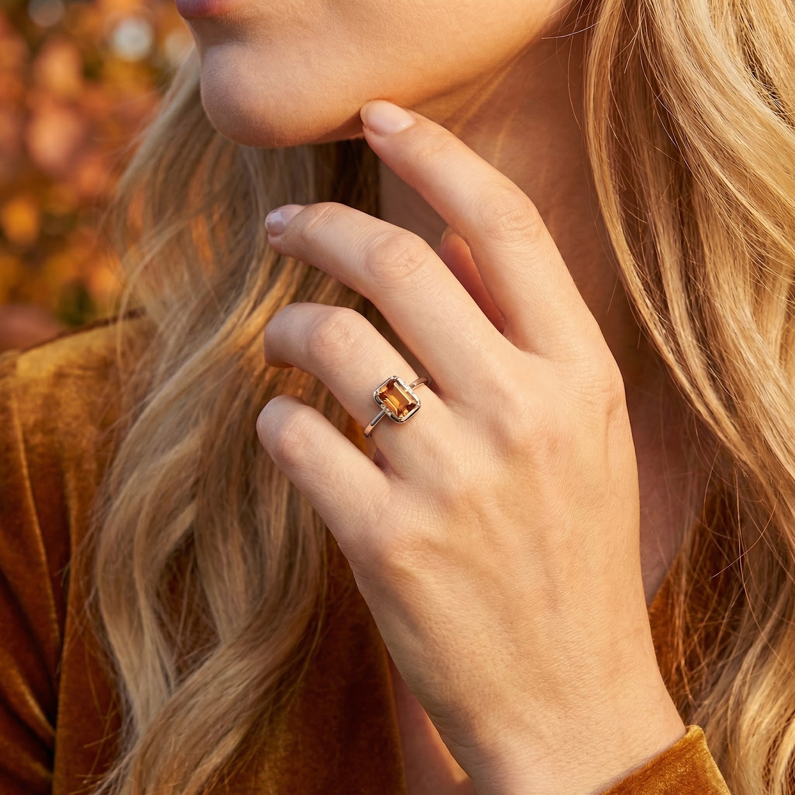 Woman wearing the Caelianna octagon simulated topaz ring in sterling silver with an autumn-themed background.