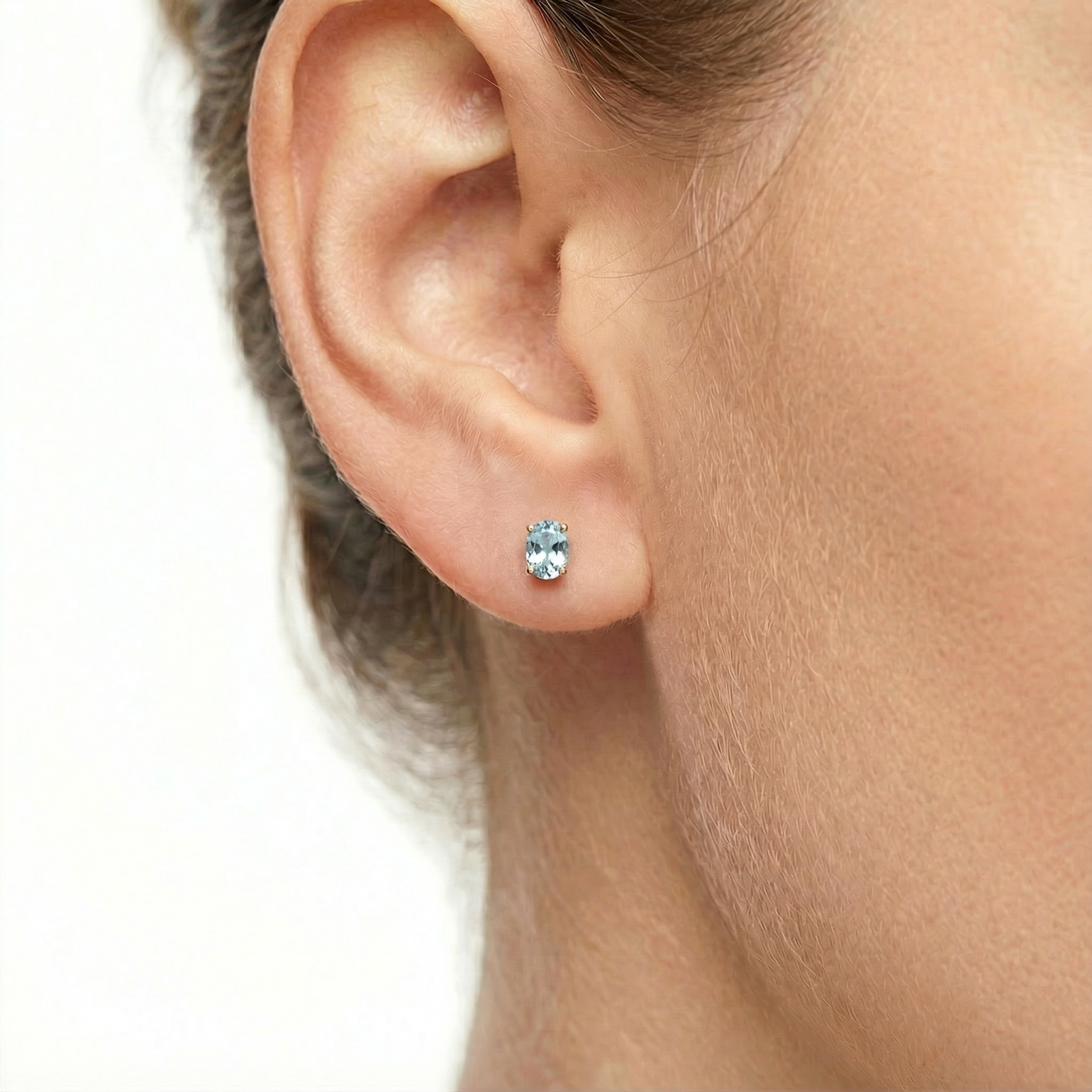 Close-up of an oval cut simulated aquamarine stud earring in 18K gold vermeil on a model's ear.