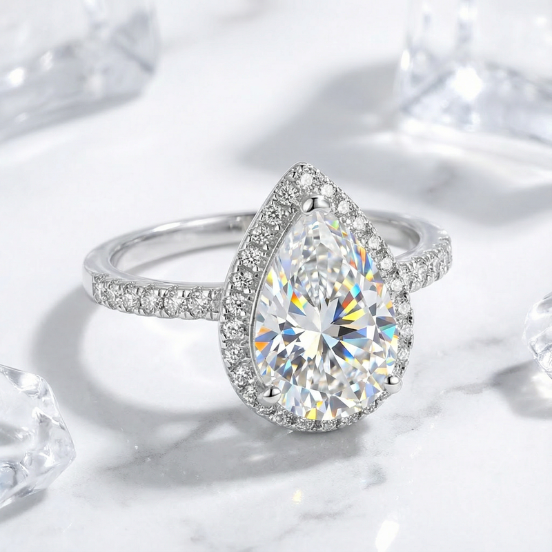 Angled side view of a pear-cut simulated diamond halo ring in S925 sterling silver on a marble background.