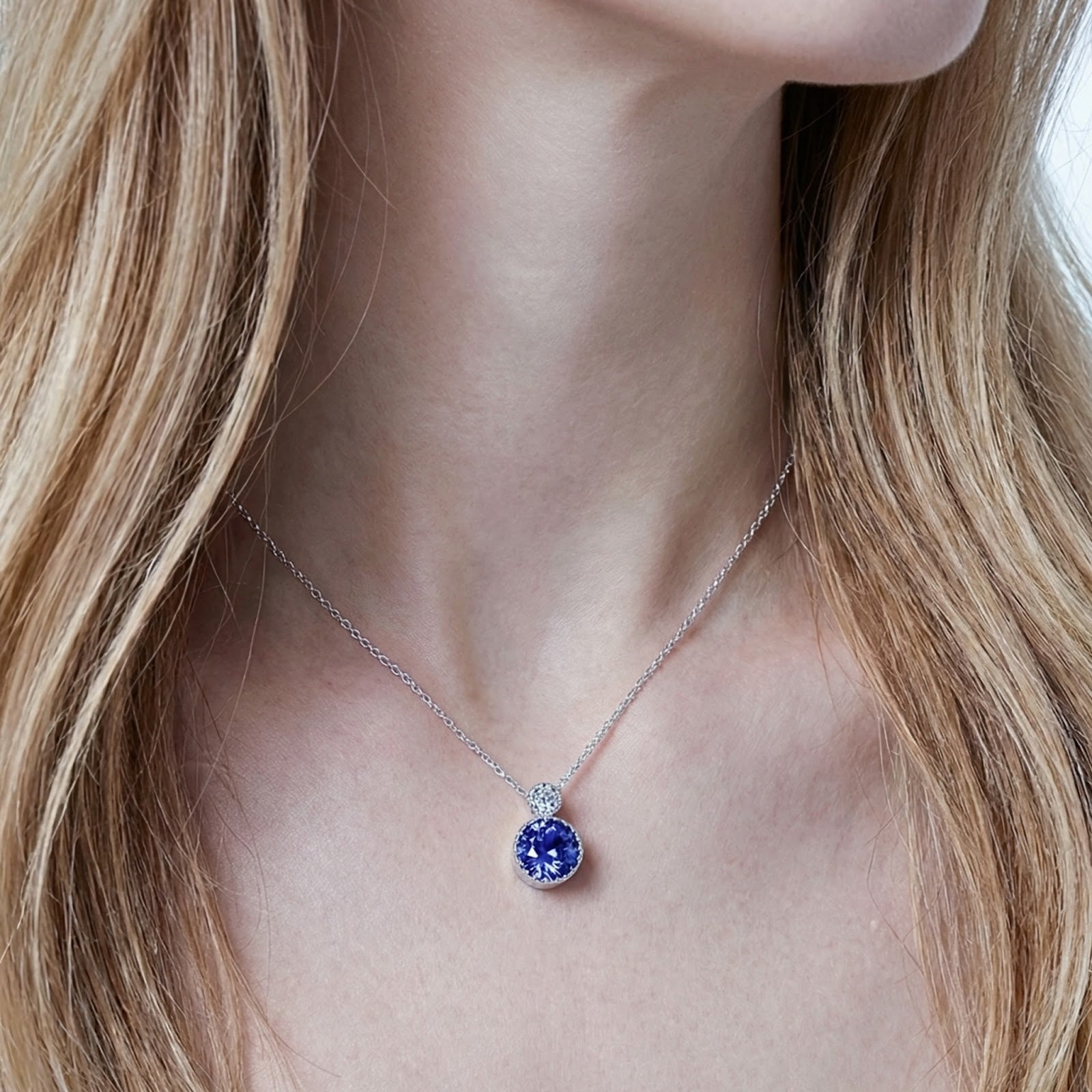Close-up of the sterling silver round-cut simulated tanzanite drop necklace worn on a woman's neck.