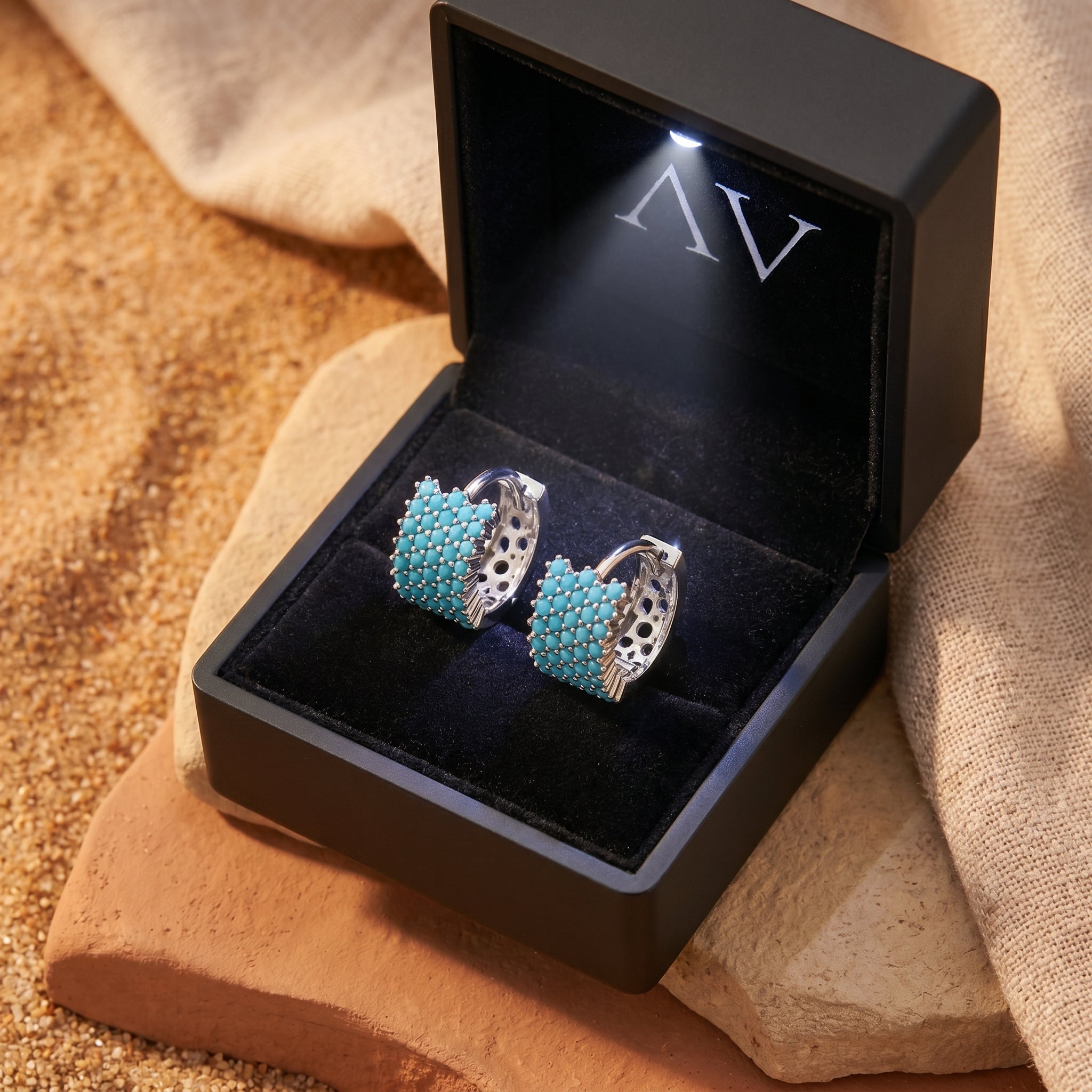 Sterling silver turquoise huggie earrings presented in a black LED-lit gift box on a desert rock.