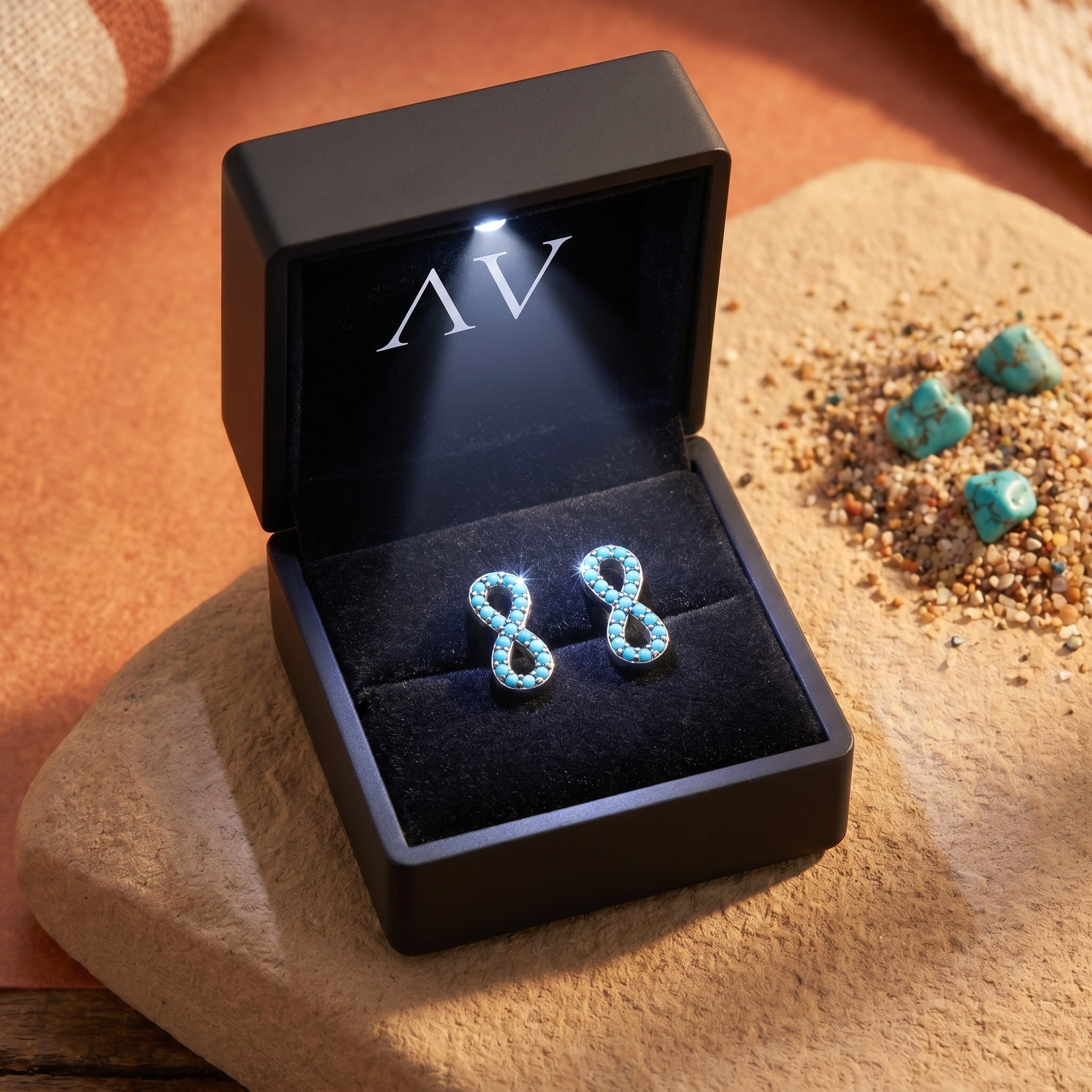 Turquoise infinity earrings in a black LED-lit jewelry presentation box on a stone surface.
