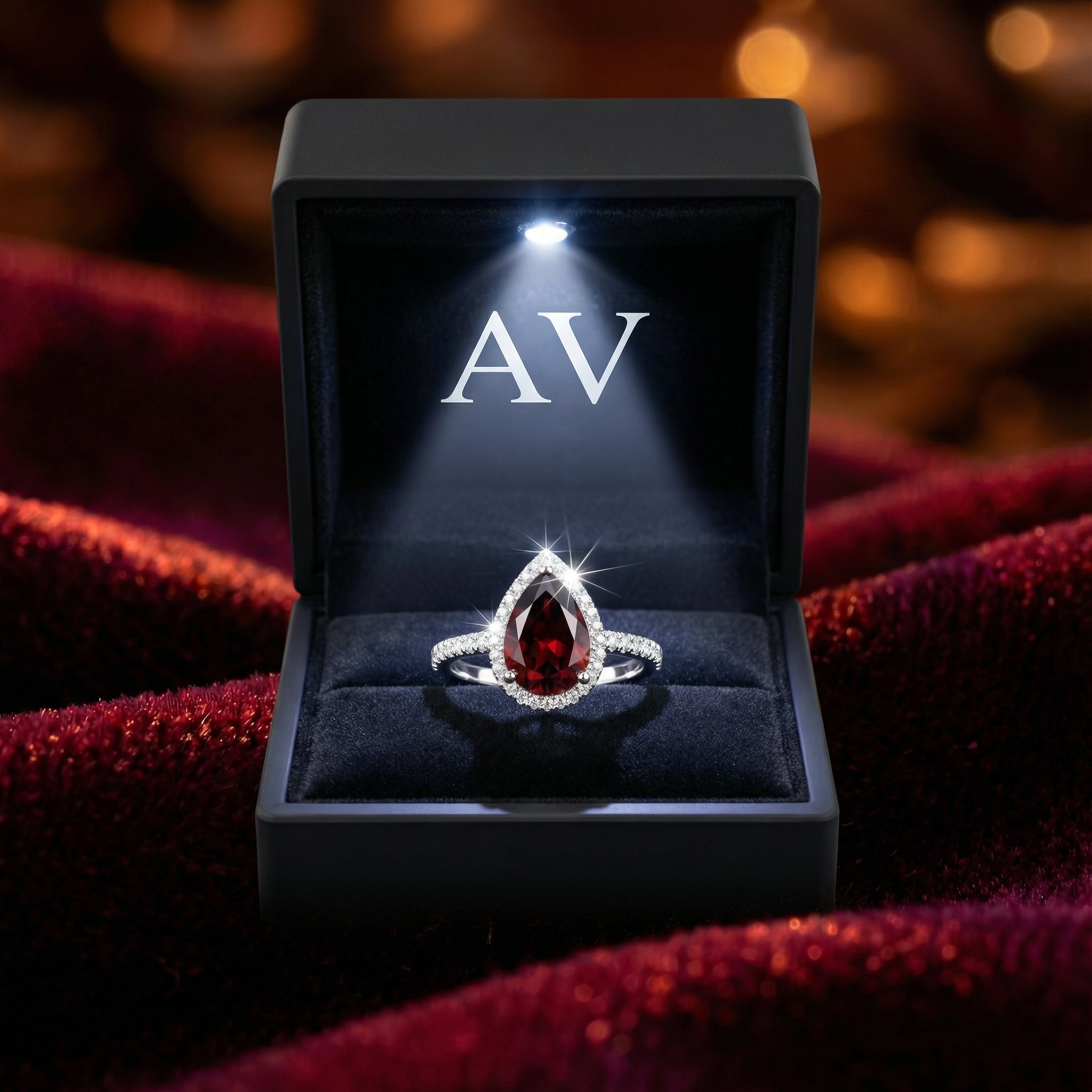 Pear-cut simulated garnet halo ring in a black LED-lit AV branded jewelry box on red velvet.