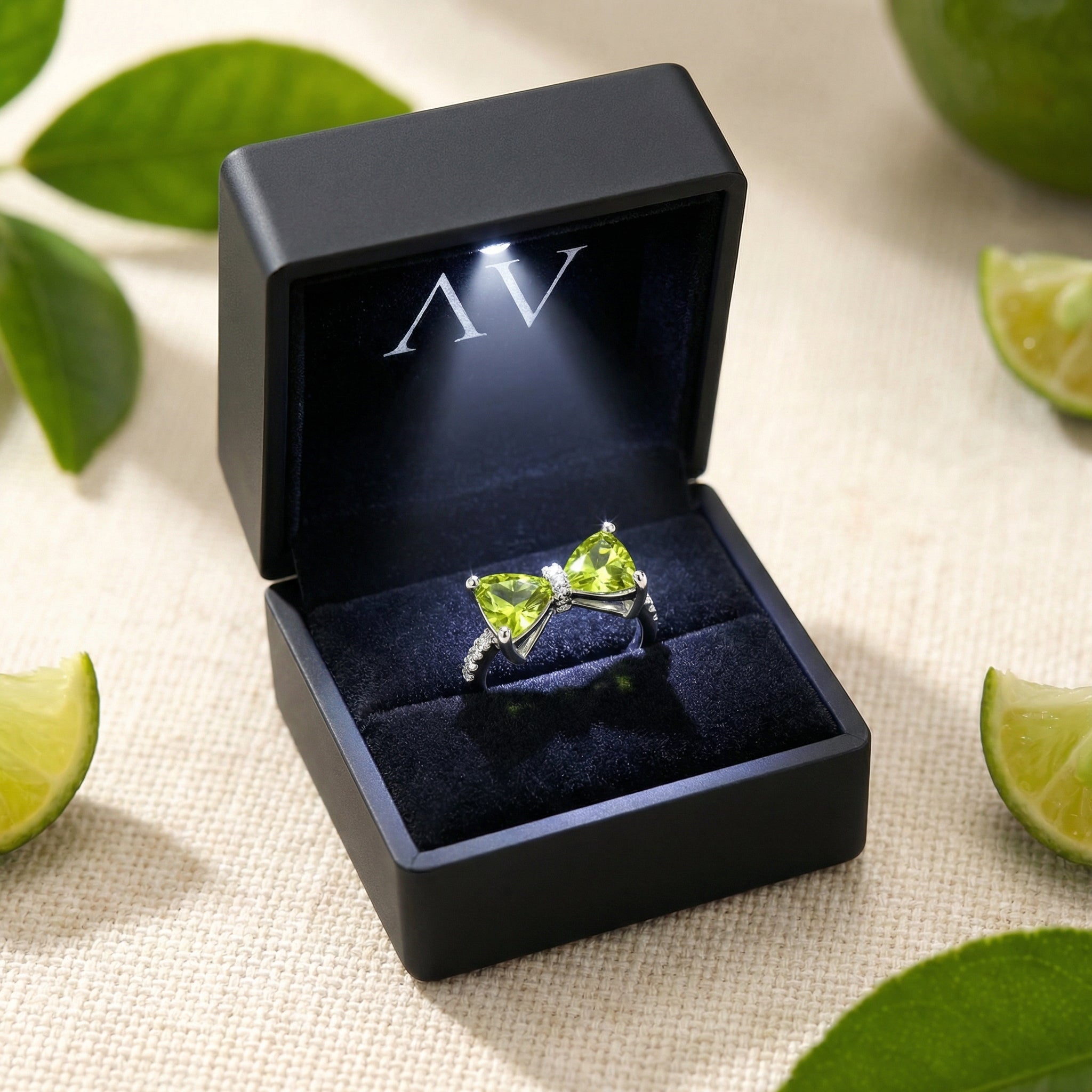 Sterling silver bow ring with green simulated peridots presented in a black lighted jewelry gift box.