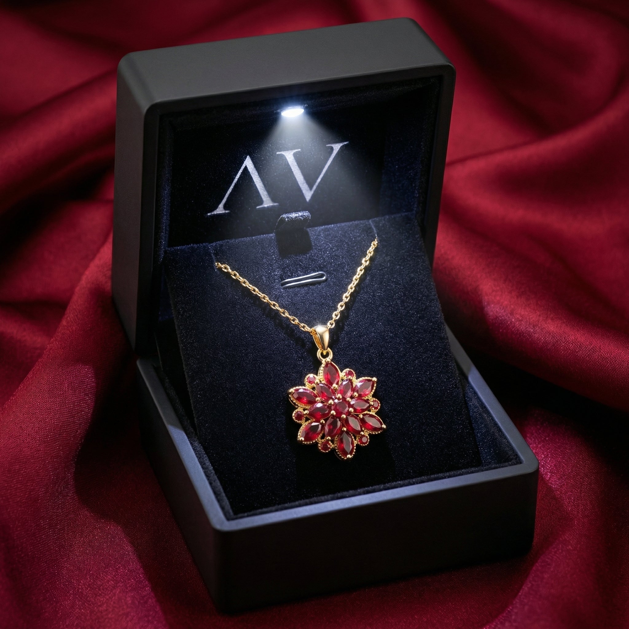 Gold stainless steel simulated ruby necklace in a black LED-lit gift box on red satin fabric.