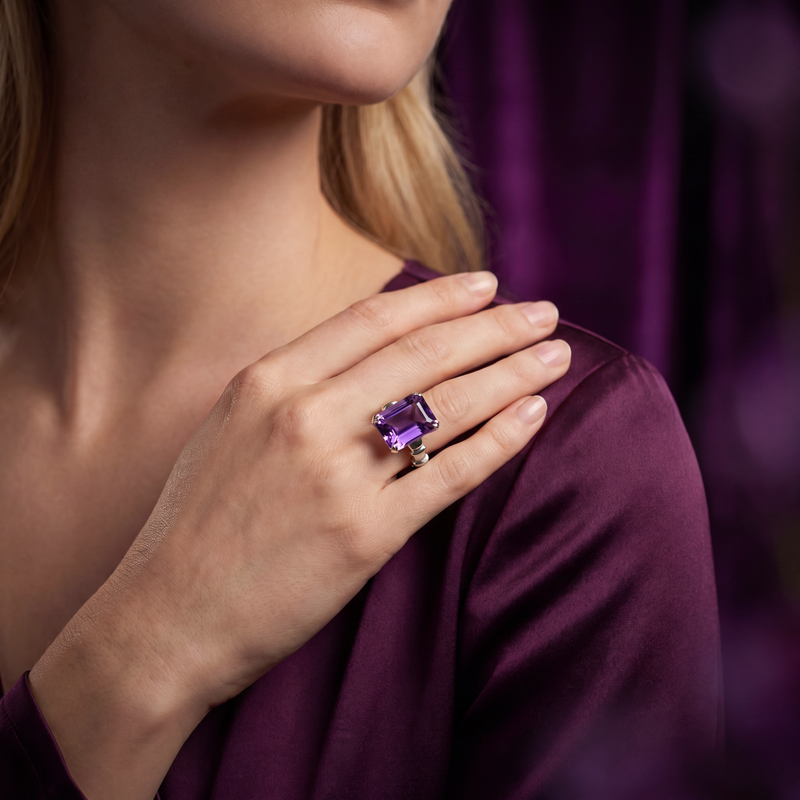 Model wearing an emerald-cut violet amethyst ring in a polished white-metal setting.