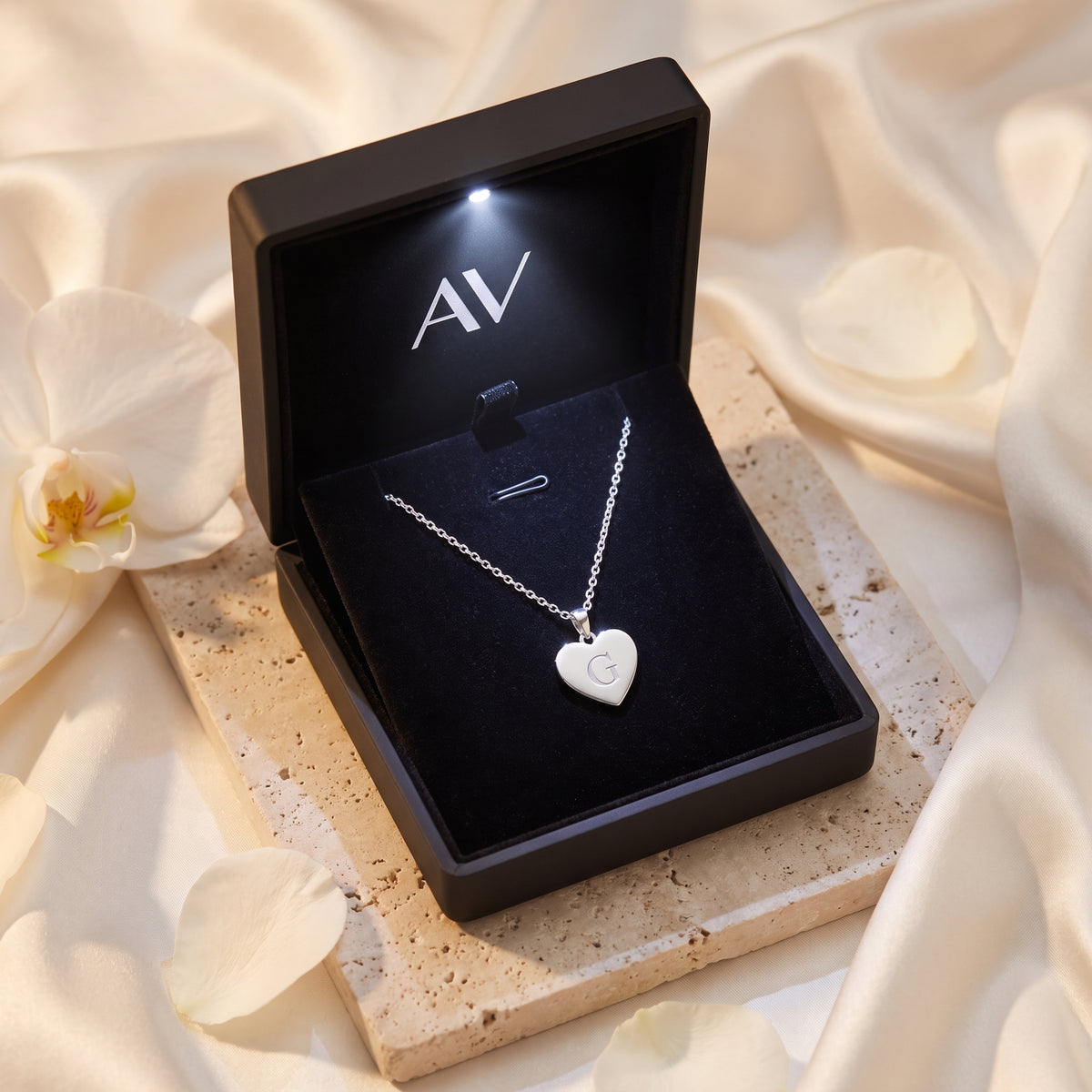 Silver heart pendant necklace with engraved 'G' inside a black LED-lit jewelry gift box.
