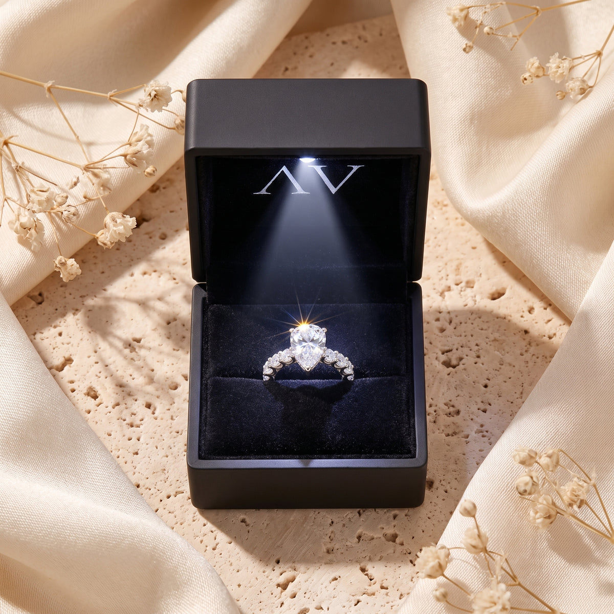 Silver pear-cut solitaire ring inside a lighted black gift box.