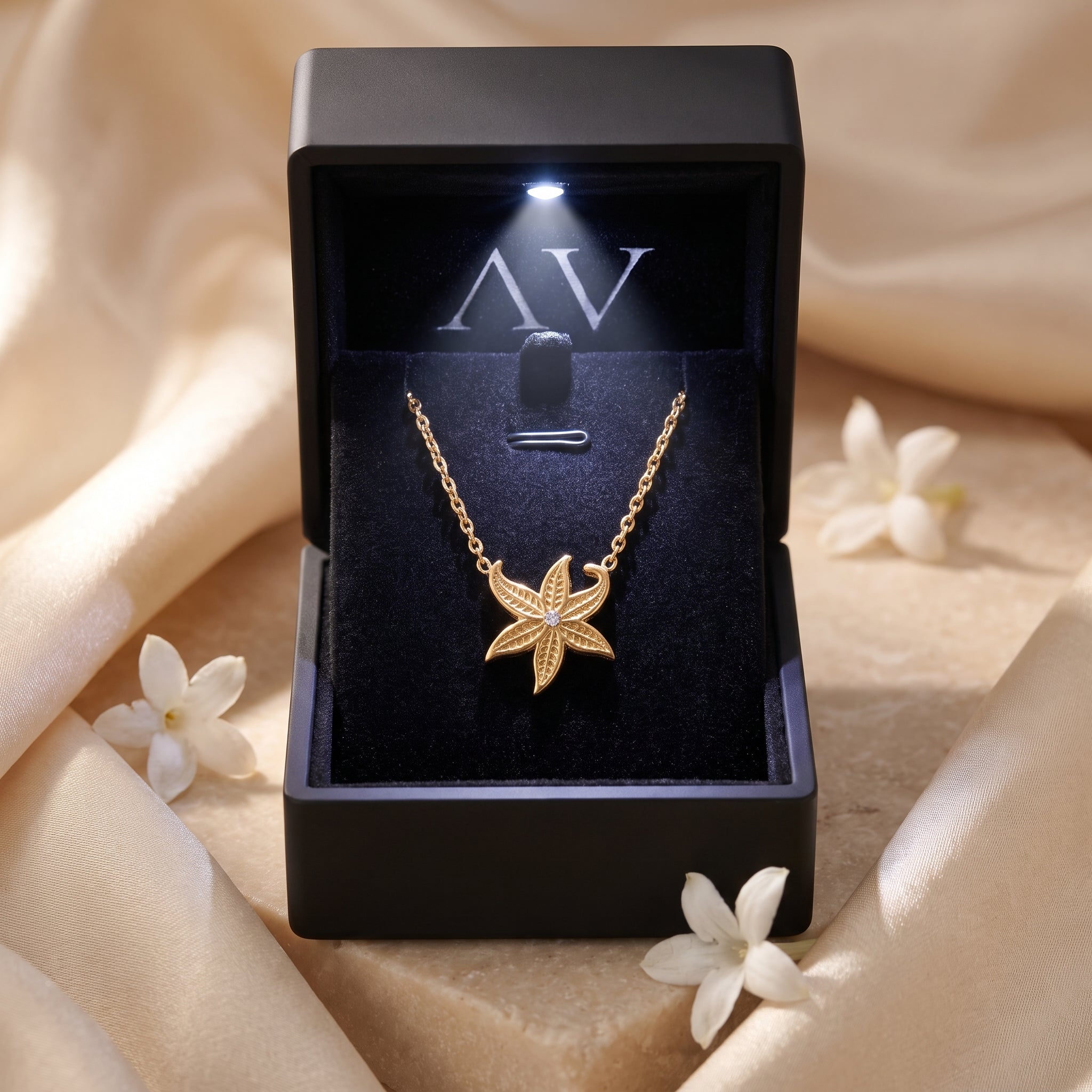 Gold starfish necklace inside a black LED-lit gift box with white flowers and silk background.