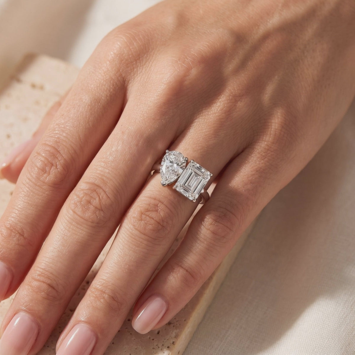 Hand wearing a silver Toi et Moi ring with pear-cut and emerald-cut clear stones