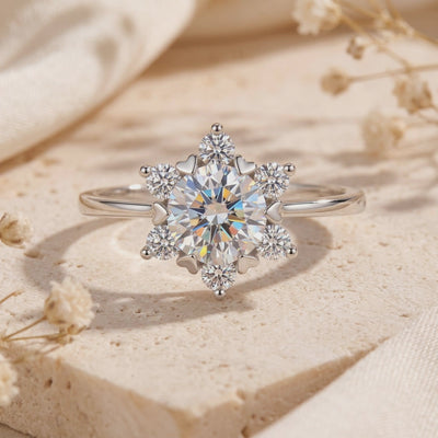 Silver snowflake cluster ring with round clear gems, resting upright on a beige stone surface.