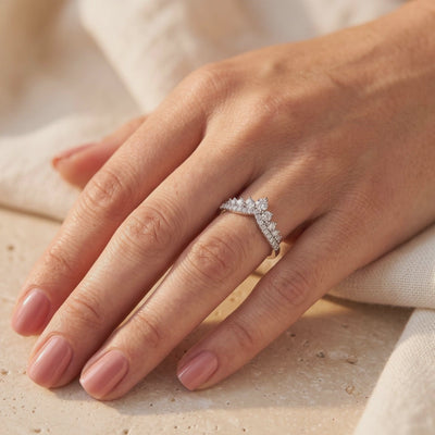Double-row silver chevron ring with clear stones worn on a hand with glossy pink nails.