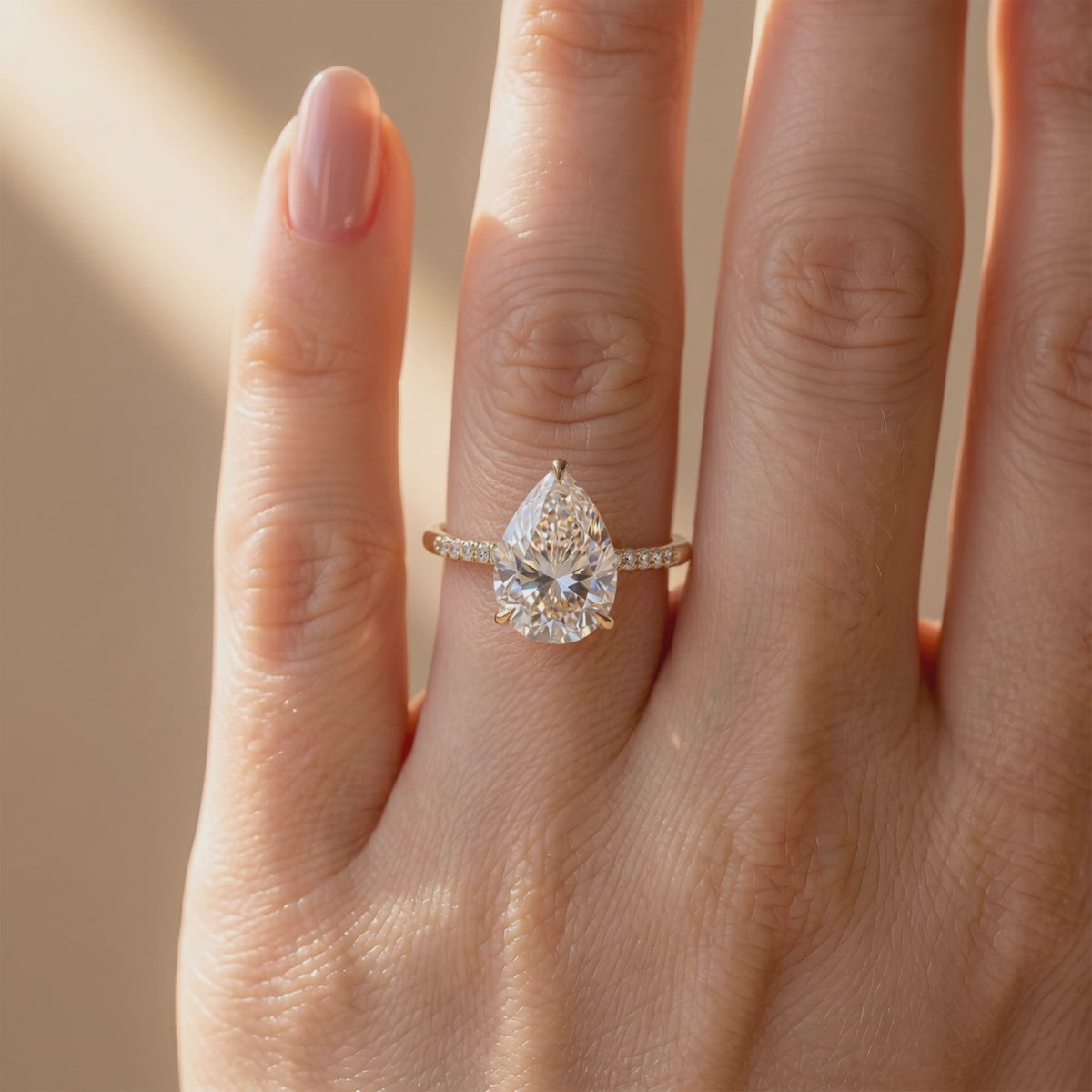 The Opaline pear-cut ring worn on a finger, shown from the front with a clear center stone and pavé band.