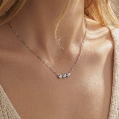Close-up of a model wearing a silver necklace with three round bezel-set moissanite stones on a fine chain.