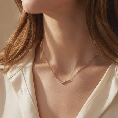 Model wearing a gold-tone chevron necklace with clear stones along her collarbone.